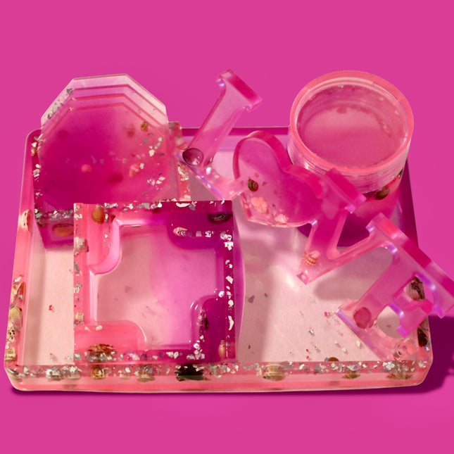 Pink and clear plastic trey set with real sea shells and glass on a pink background